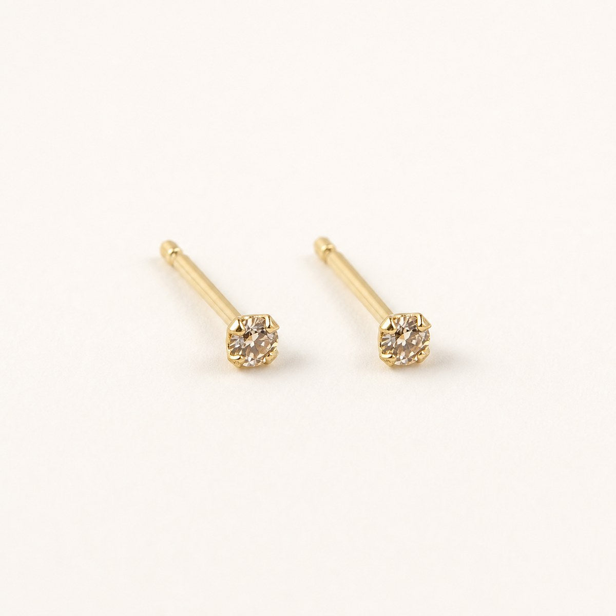 14K solid gold petite bezel solitaire stud earrings on a warm ivory background
