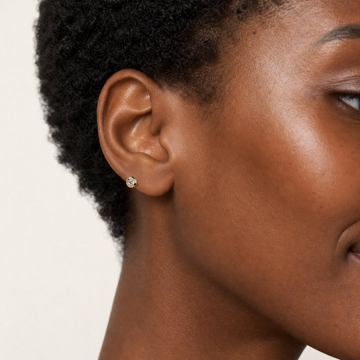14K solid gold bezel floral halo stud earrings worn on an ear