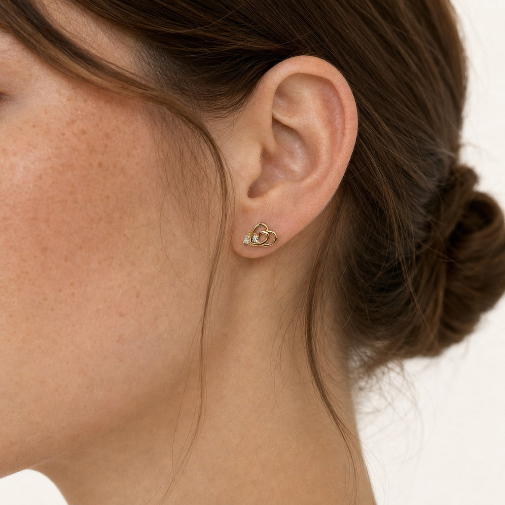 14K solid gold double heart stud earrings worn on an ear