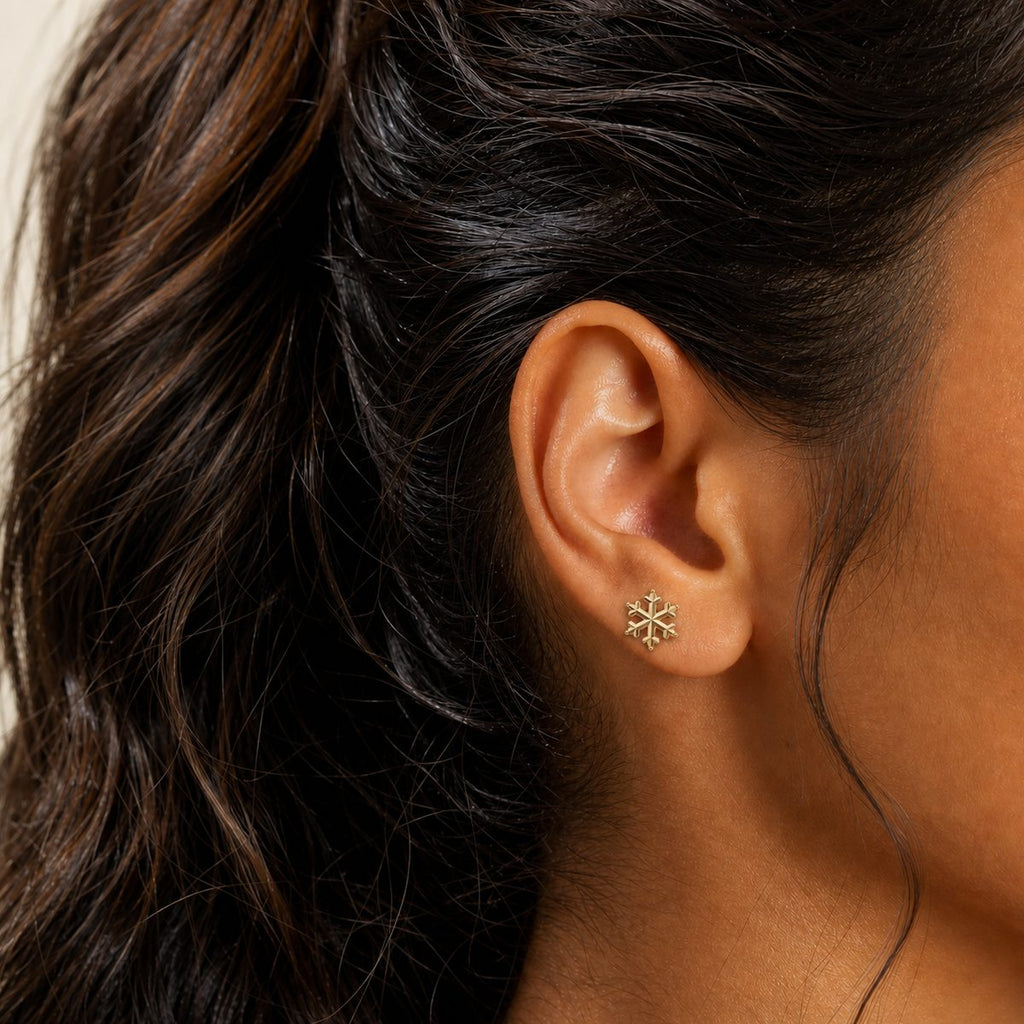 14K solid gold textured snowflake stud earrings worn on an ear