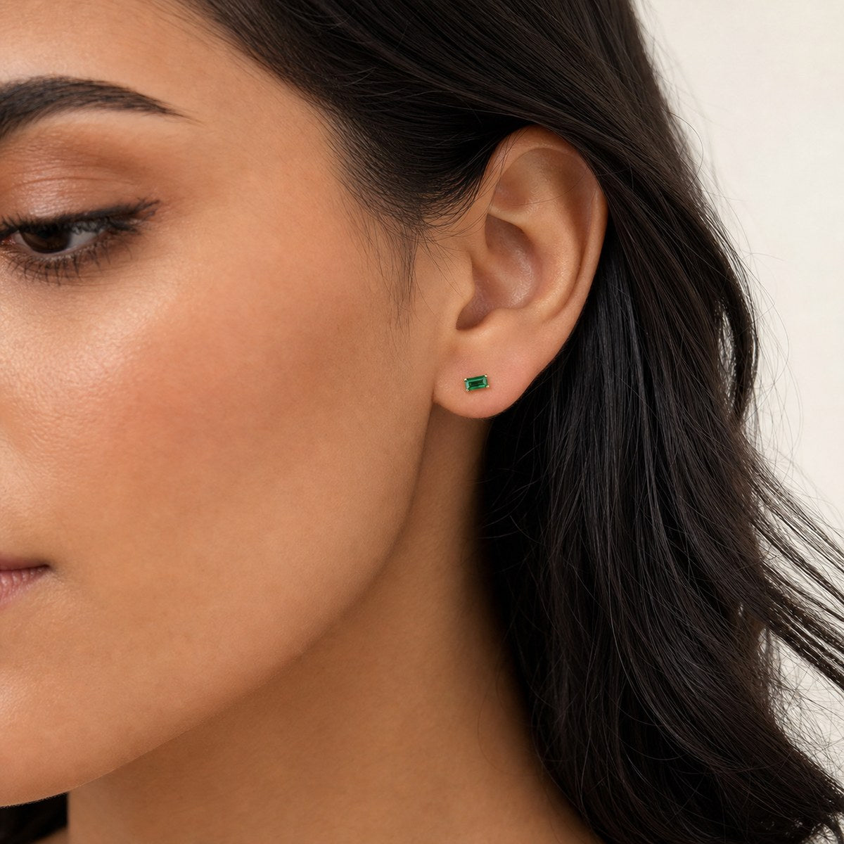 14K solid gold green emerald cut stud earrings worn on an ear