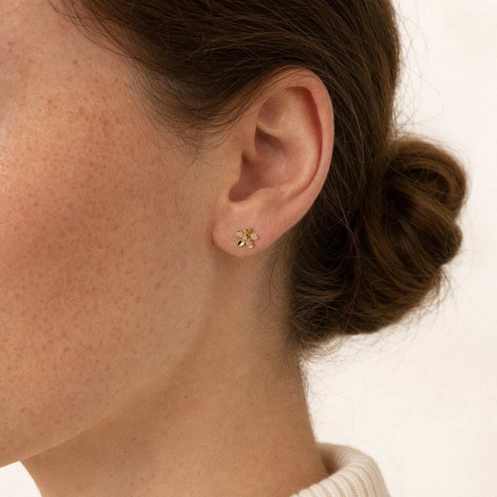 14K solid gold open petal flower stud earrings worn on an ear