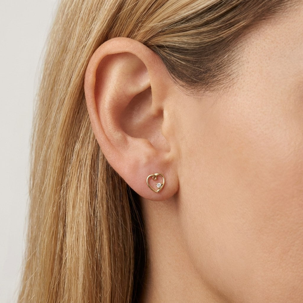 14K solid gold swirl heart stud earrings worn on an ear