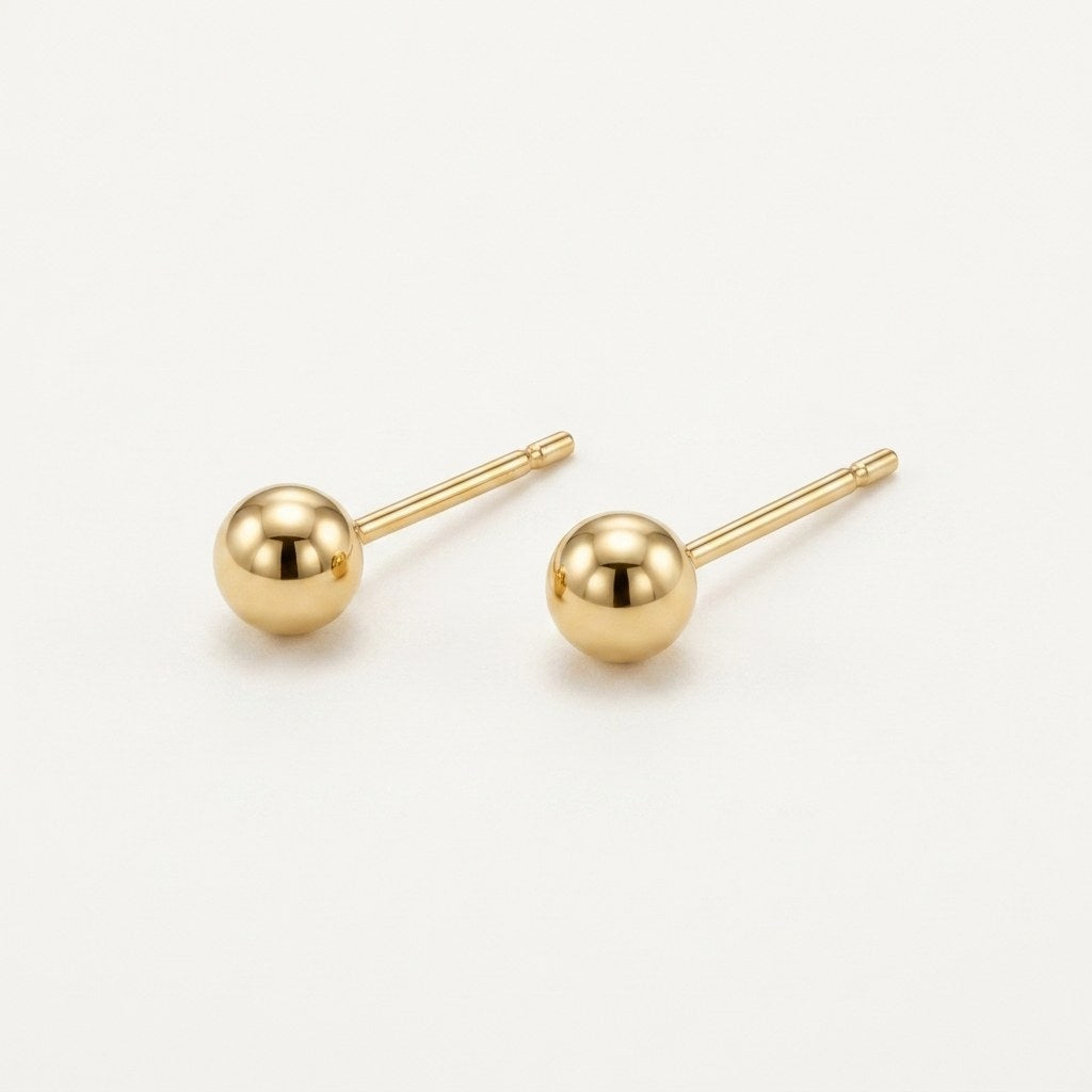 14K solid gold polished gold ball stud earrings on a warm ivory background