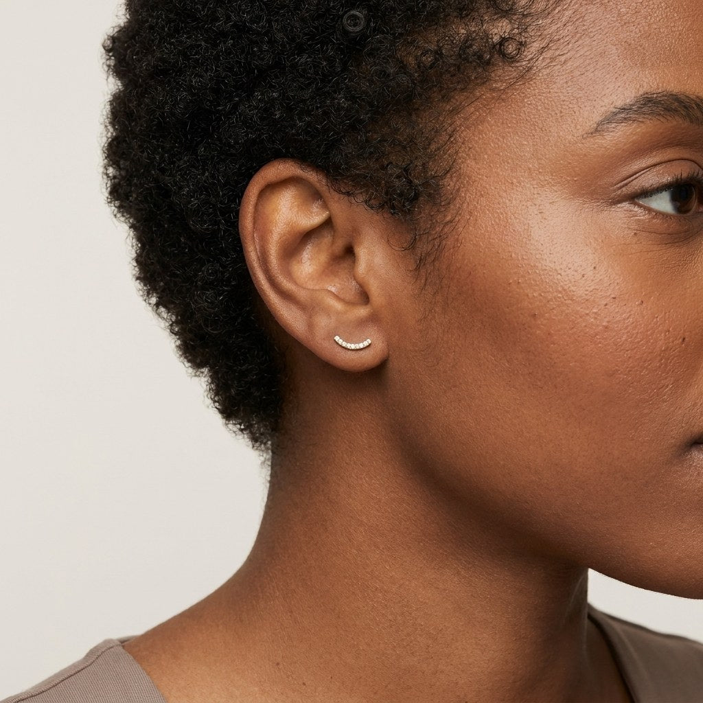 14K solid gold curved pave bar stud earrings worn on an ear