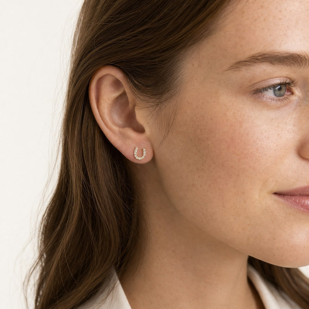 14K solid gold crystal horseshoe stud earrings worn on an ear