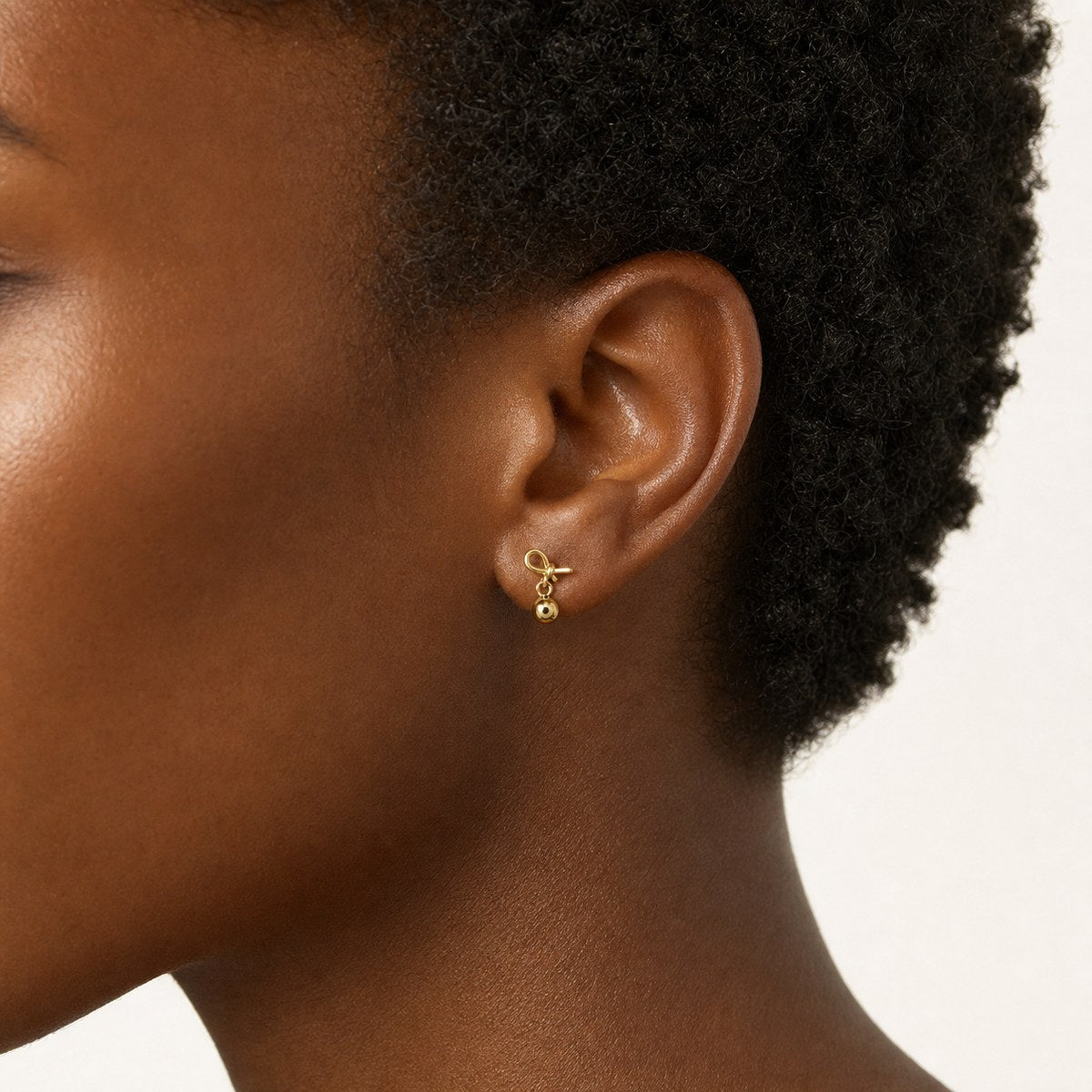 14K solid gold bow ball drop stud earrings worn on an ear