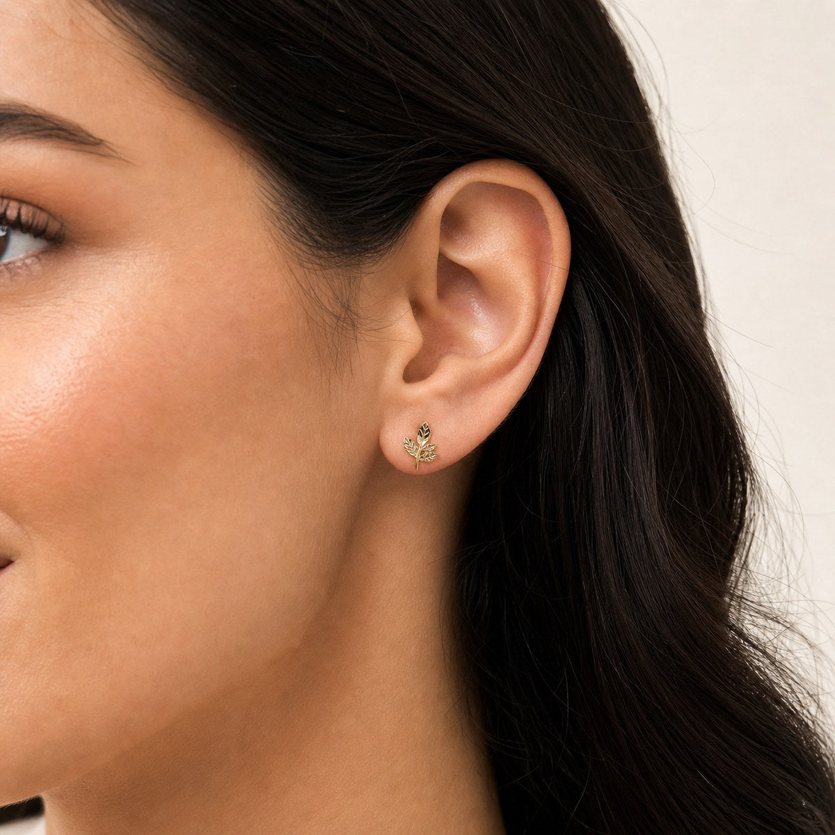 14K solid gold textured leaf branch stud earrings worn on an ear