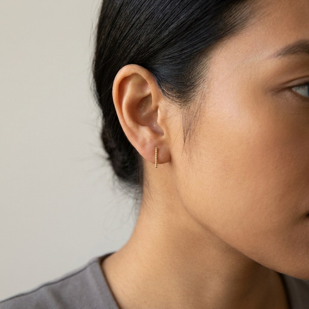 14K solid gold beaded bar stud earrings worn on an ear