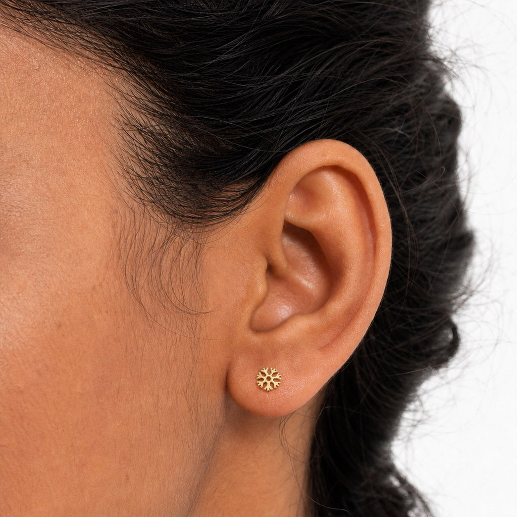 14K solid gold cutout snowflake stud earrings worn on an ear
