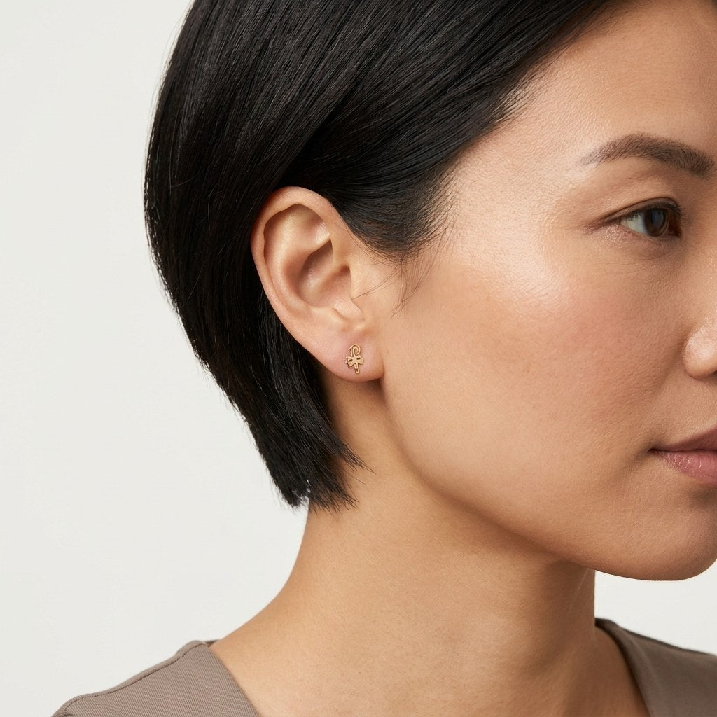 14K solid gold abstract script stud earrings worn on an ear