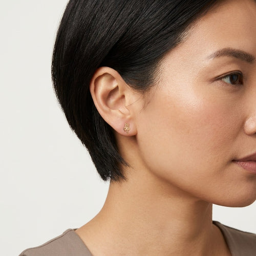 14K solid gold abstract script stud earrings worn on an ear