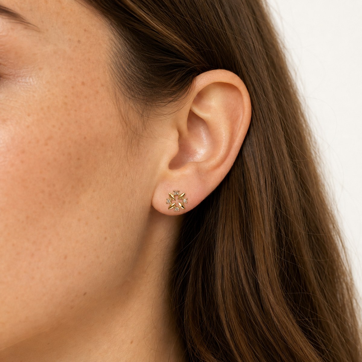14K solid gold crystal pinwheel flower stud earrings worn on an ear