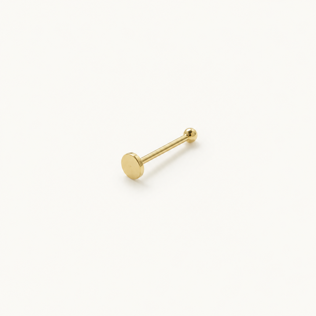 Solid Gold Flat Disc Nose Stud in yellow gold on a warm ivory background