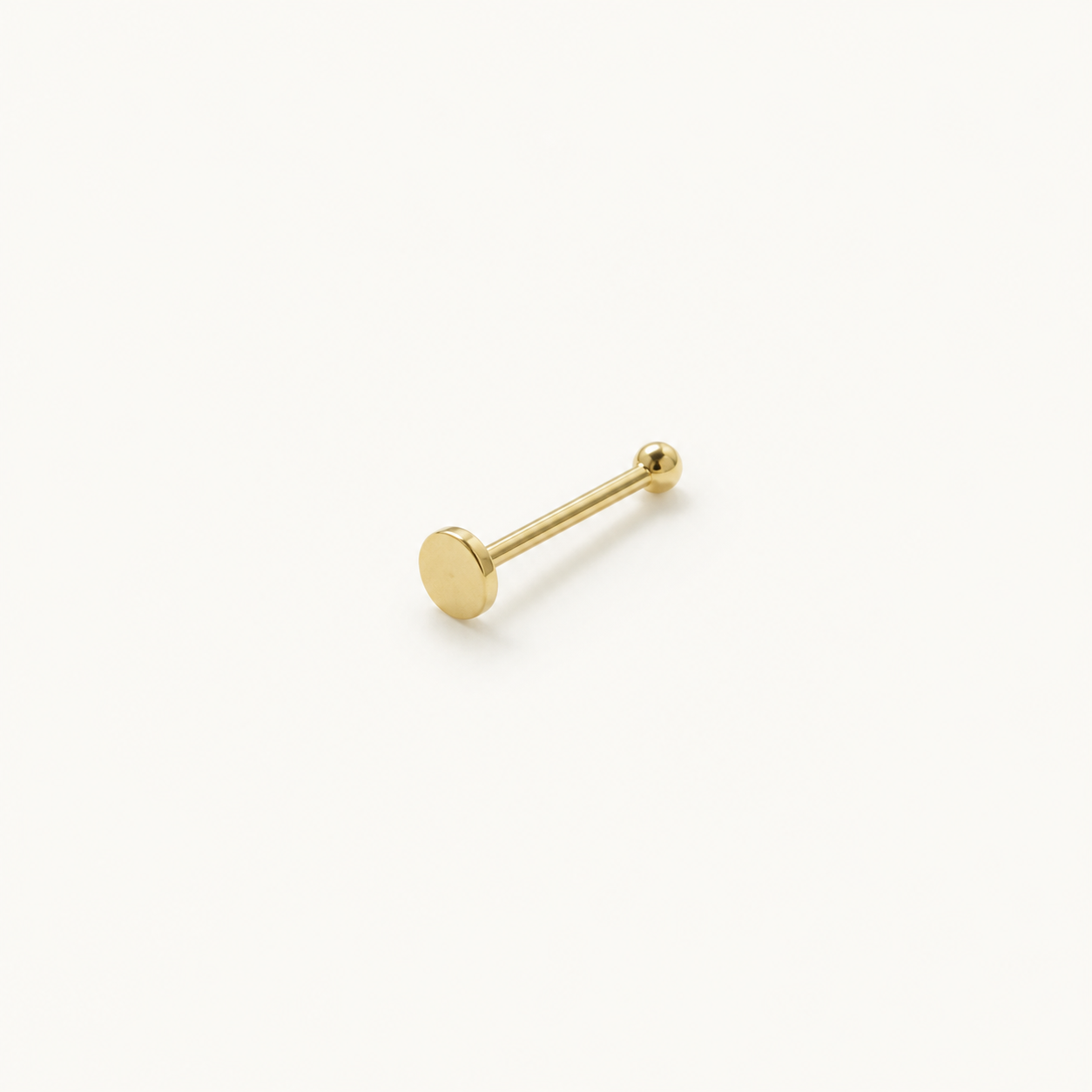 Solid Gold Flat Disc Nose Stud in yellow gold on a warm ivory background